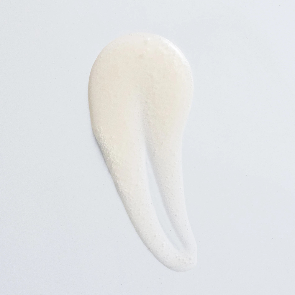 Creamy white clarifying shampoo swatch with small bubbles on a white background.