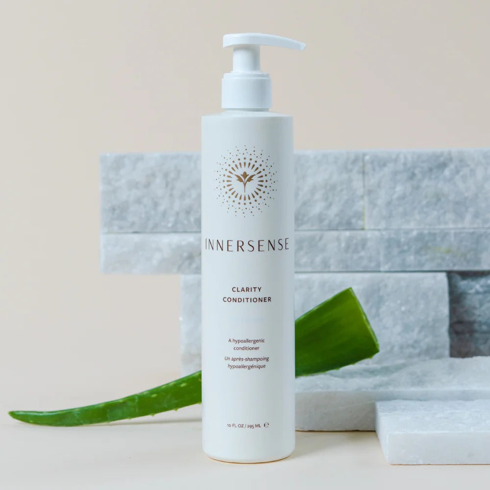 White Innersense Clarity Conditioner pump bottle with gold logo, aloe leaf, and white marble blocks.