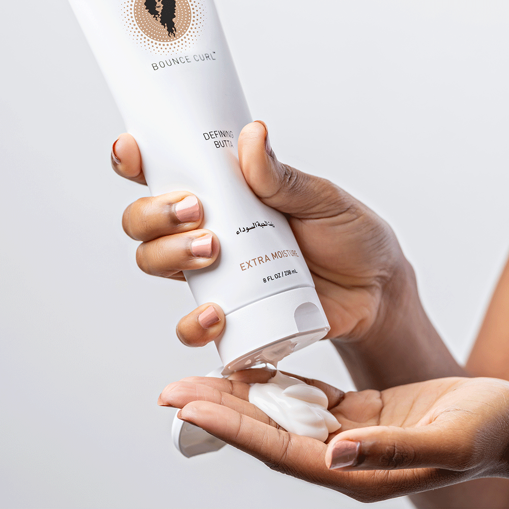 Hands squeezing white Bounce Curl Defining Butta from a tube into a palm.