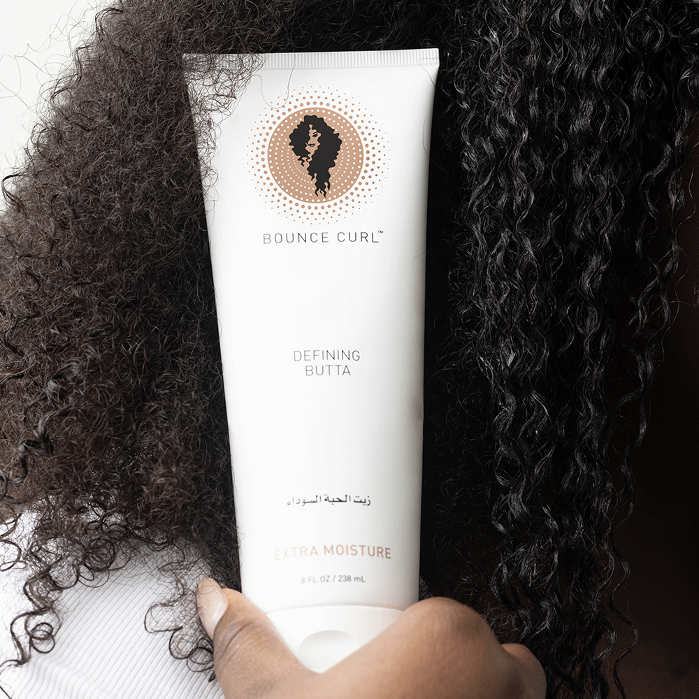 Bounce Curl Defining Butta in a white tube held against dark, coily hair.