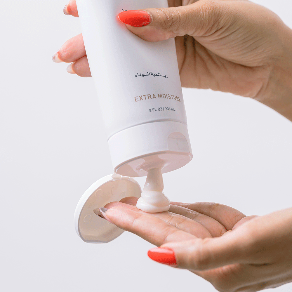 Hands with red nails squeezing white Bounce Curl Defining Butta 238ml cream onto a palm.