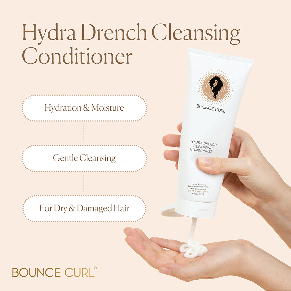 Hand squeezing white Bounce Curl Hydra-Drench Cleansing Conditioner tube, dispensing creamy product.