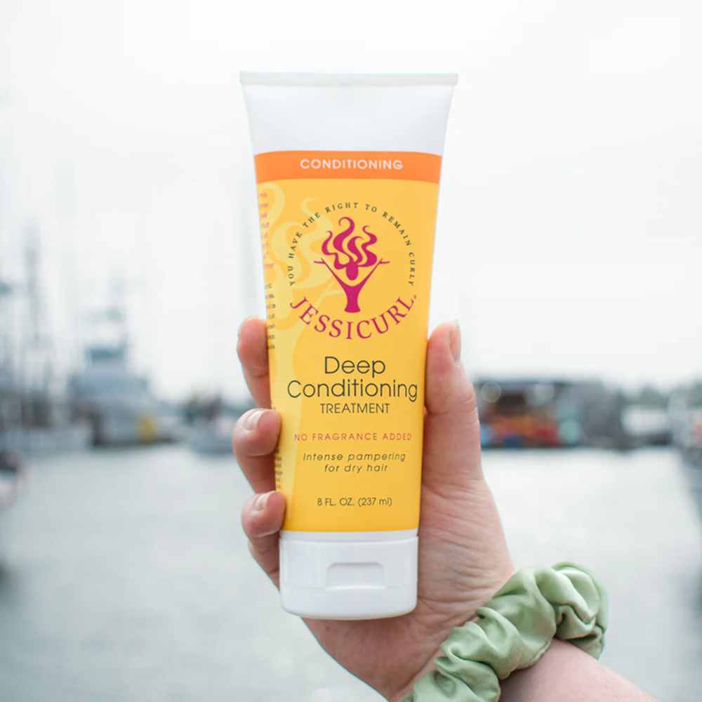 Hand holding a yellow Jessicurl Deep Conditioning Treatment tube with orange accents, 8 fl oz.