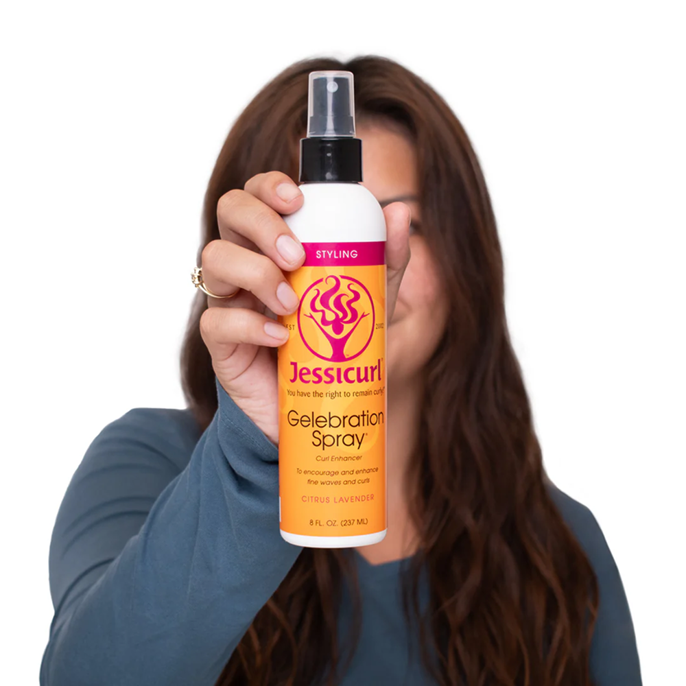 Woman holding a white Jessicurl Gelebration Spray bottle with orange and pink label.