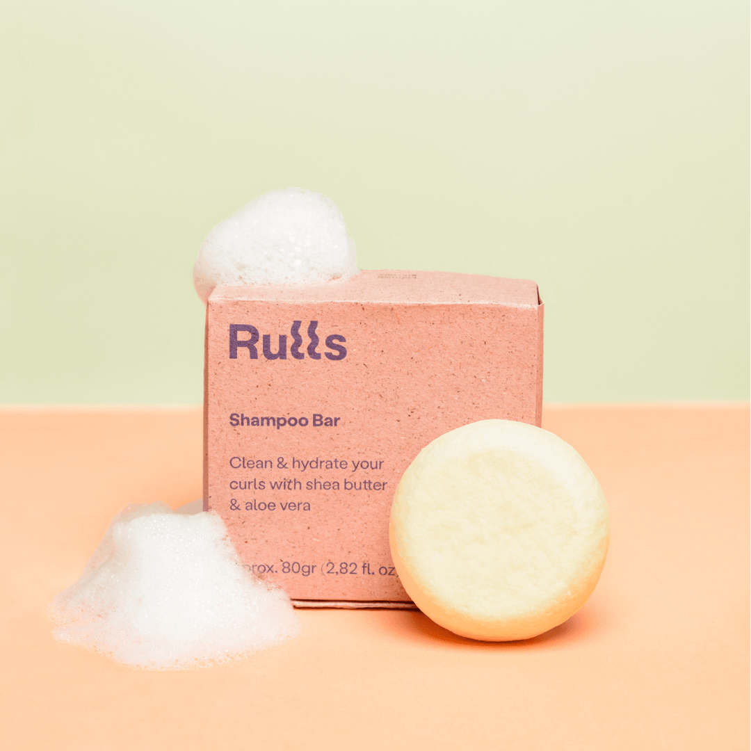 Rulls Solid Shampoo Bar, 80g, in light yellow, next to its pink paper box with white foam.
